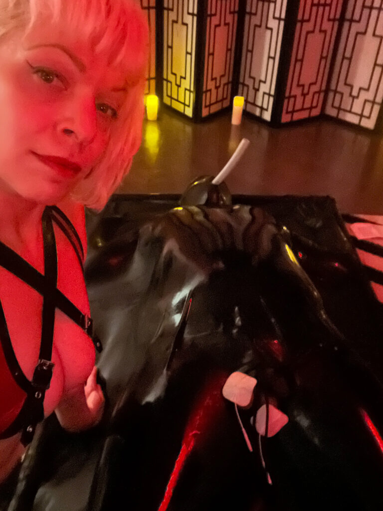 Latex dominatrix polishing latex gear in private BDSM playspace in Philadelphia.